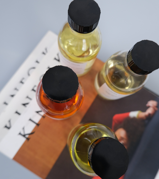 A top-down view of hand-poured botanical scent formulations in glass vessels, styled cleanly on a minimalist print publication to showcase the premium amber tones of the liquid.