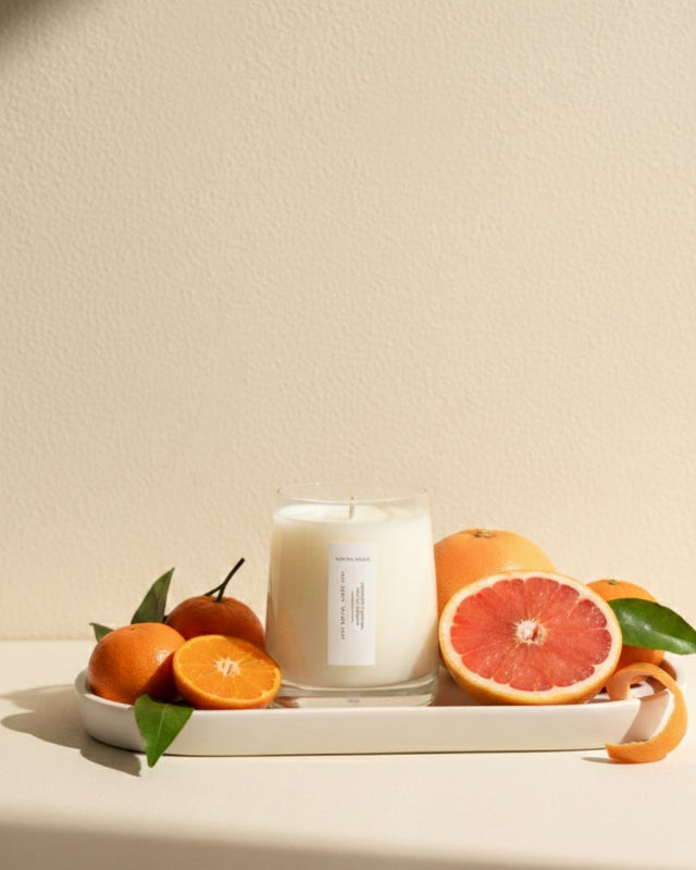 Mayowa Samuel "Less Stress More Zest" aromatherapy candle surrounded by fresh pink grapefruit and mandarin oranges. A refreshing scent profile of mandarin, grapefruit, and tea tree
