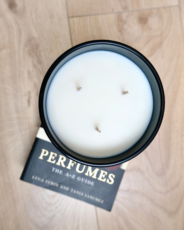 Top-down aerial view of MAYOWA SAMUEL 650g large 3-wick hand-poured candle placed over Perfumes The A-Z Guide book.