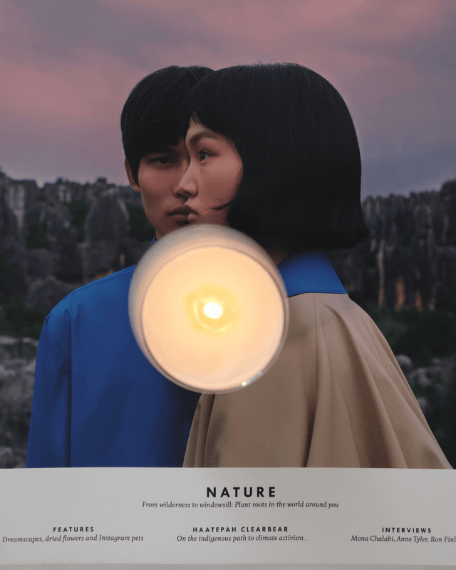 A glowing candle with a steady flame sitting atop a Kinfolk magazine, highlighting a clean, serene, and modern aesthetic